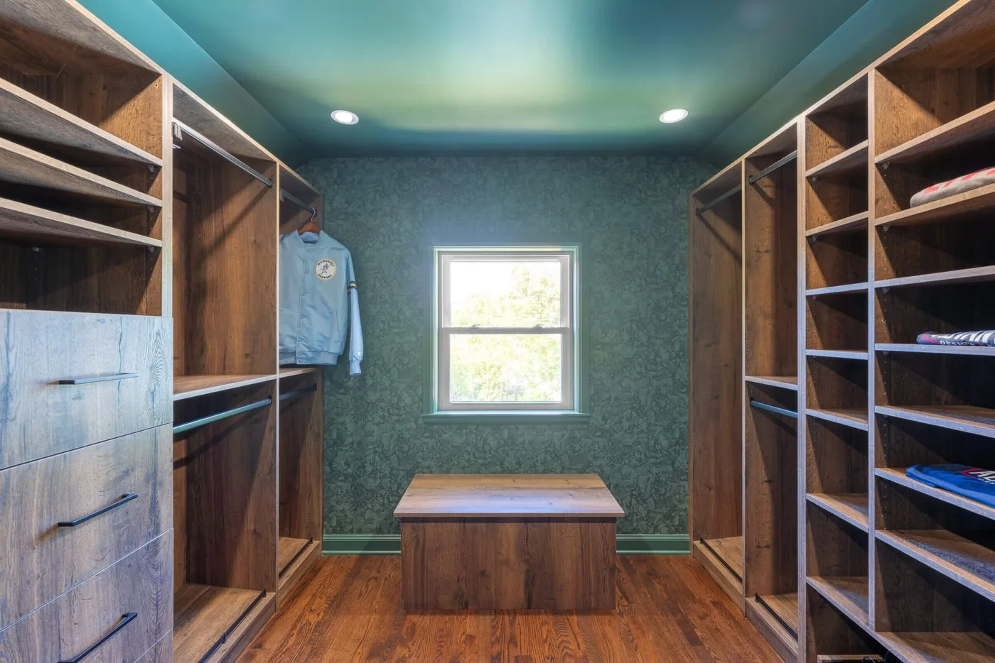 Walk in closet with open shelving, hanging rods, and a window at the far end