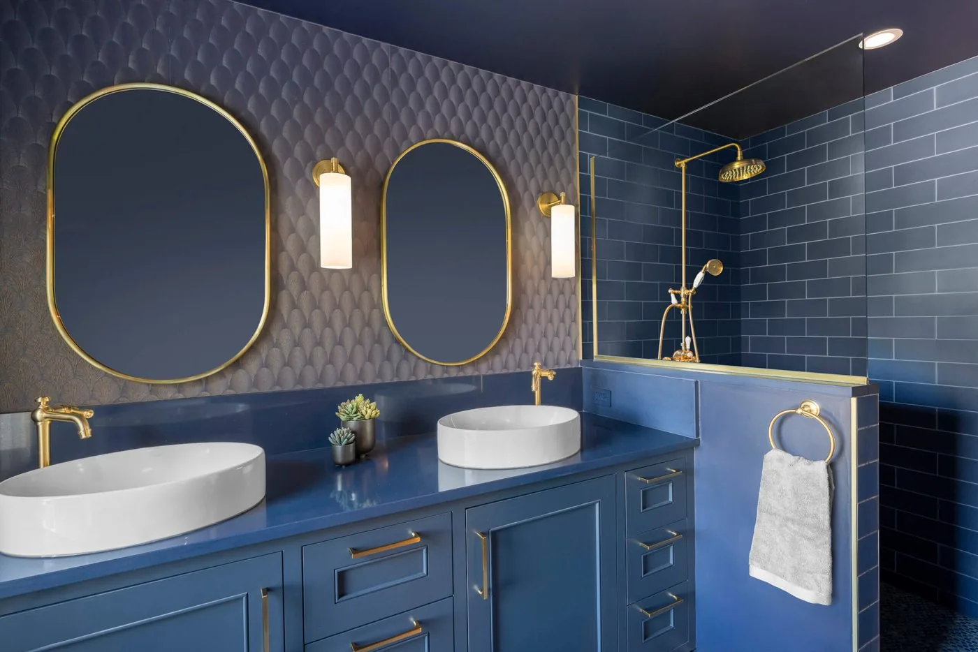 Bathroom in deep blue tile with brass fittings, twin vessel sinks, and oval mirrors